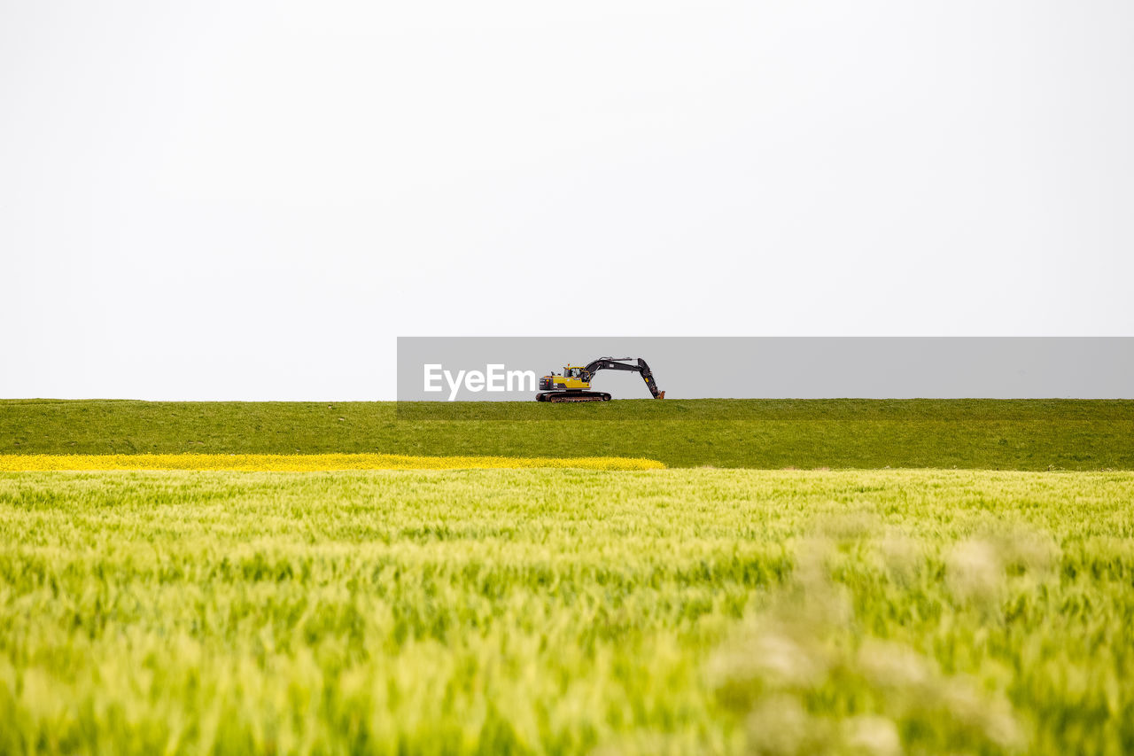 Excavator on grassy field against clear sky