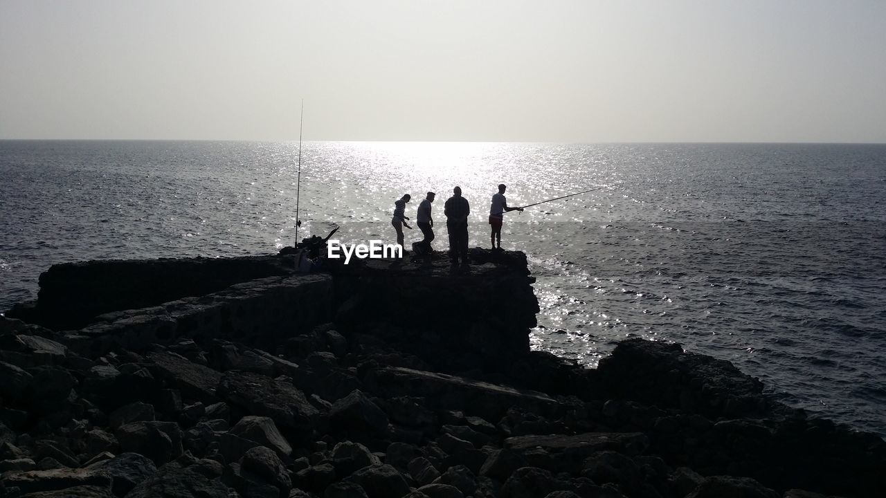 Silhouette people fishing in sea against sky