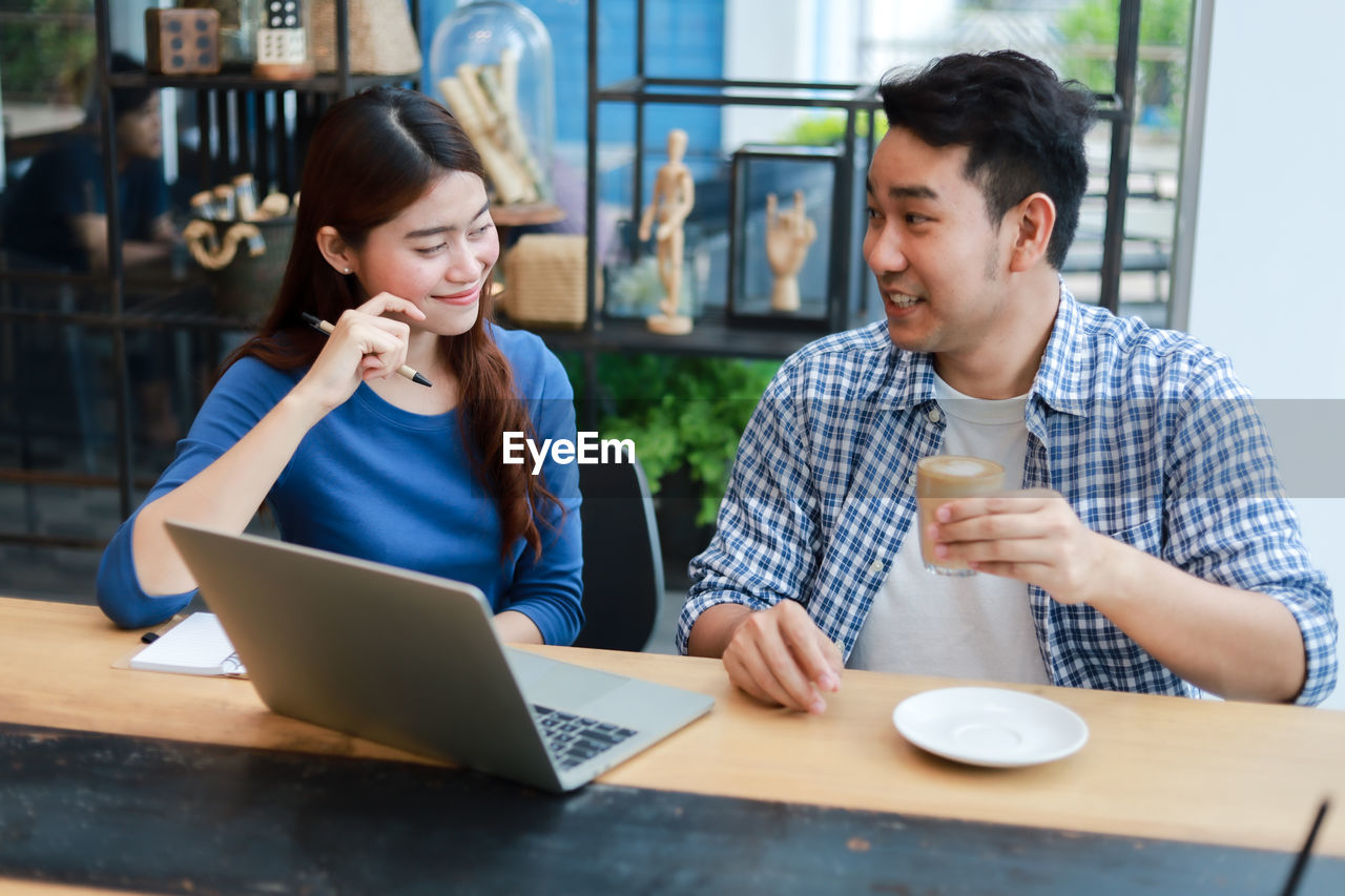 YOUNG WOMAN USING PHONE WHILE SITTING AT TABLE