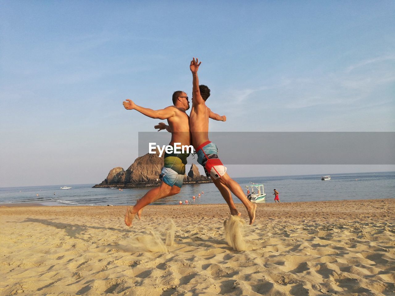 Side view of male friends chest bumping while enjoying at beach against sky