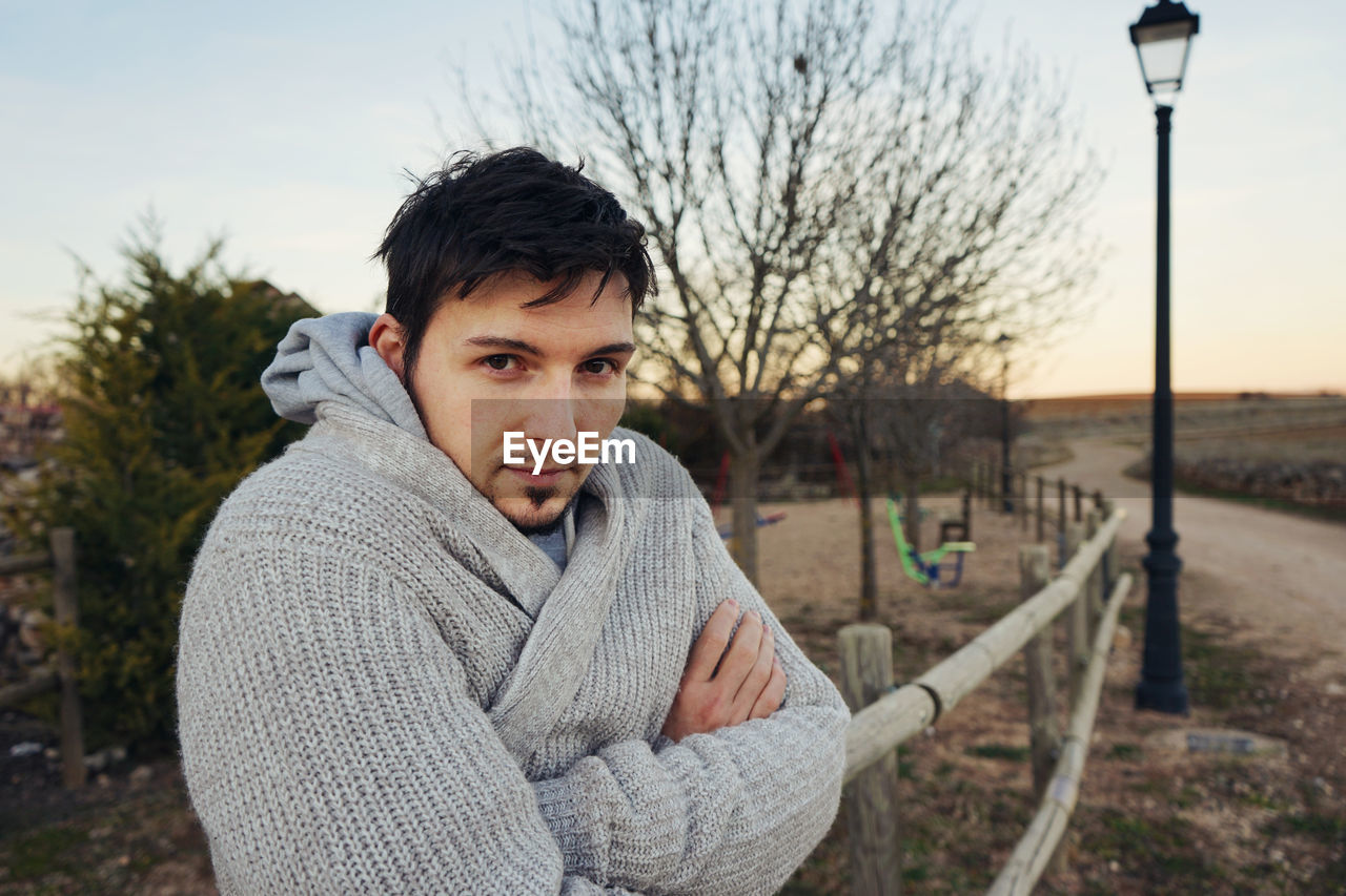 Portrait of man wearing warm clothing by railing during sunset