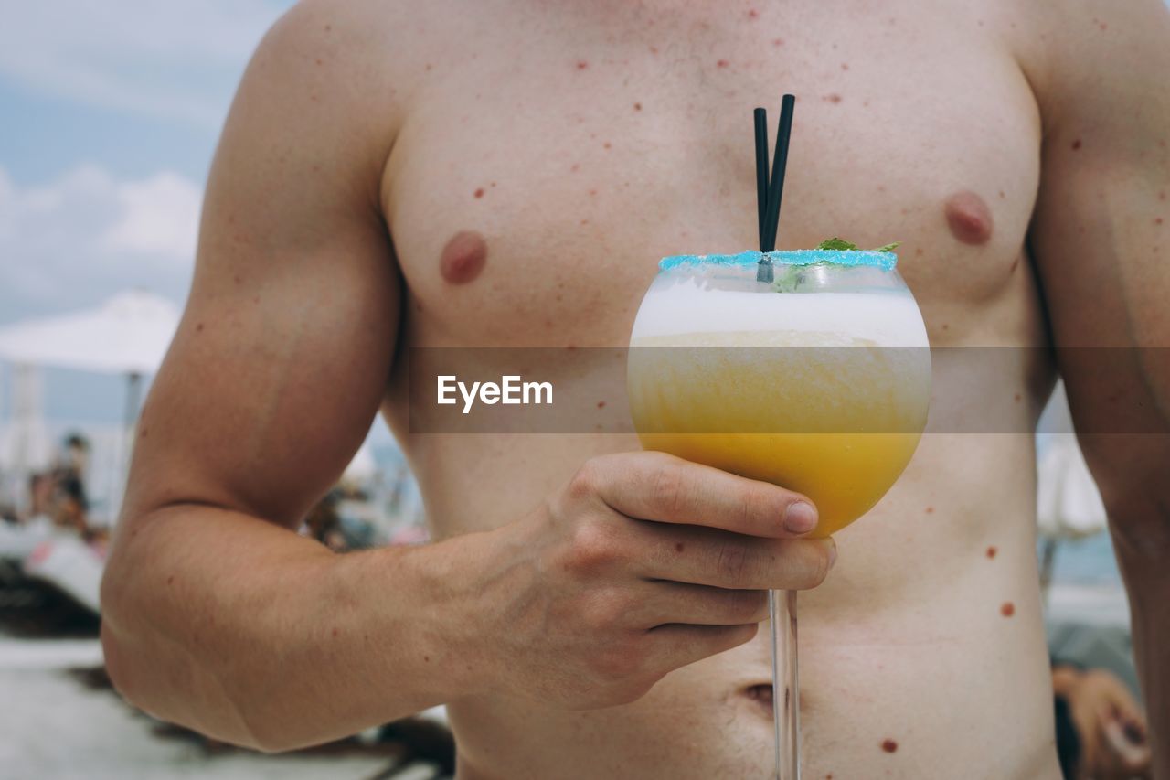 Midsection of shirtless man holding drink