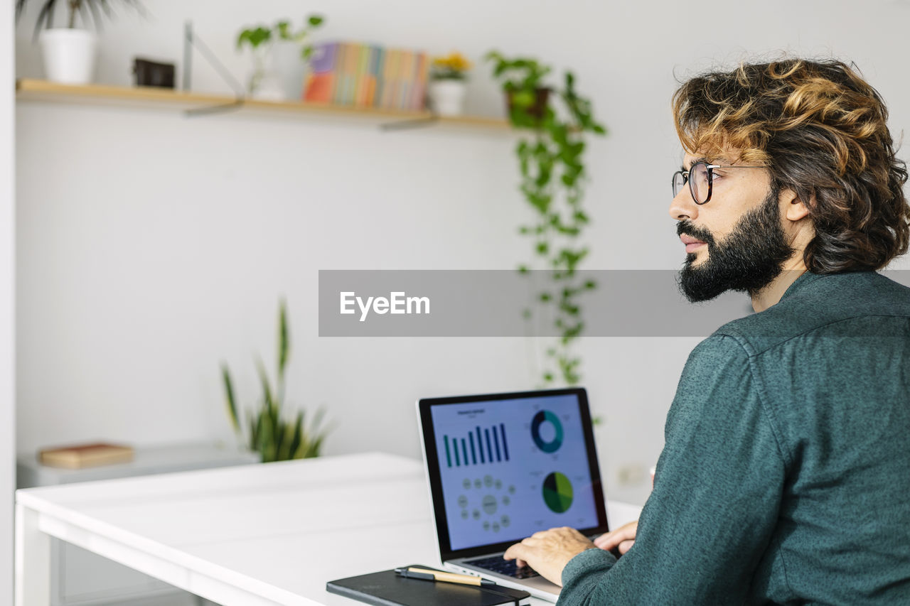 Thoughtful mature freelancer with laptop sitting at desk