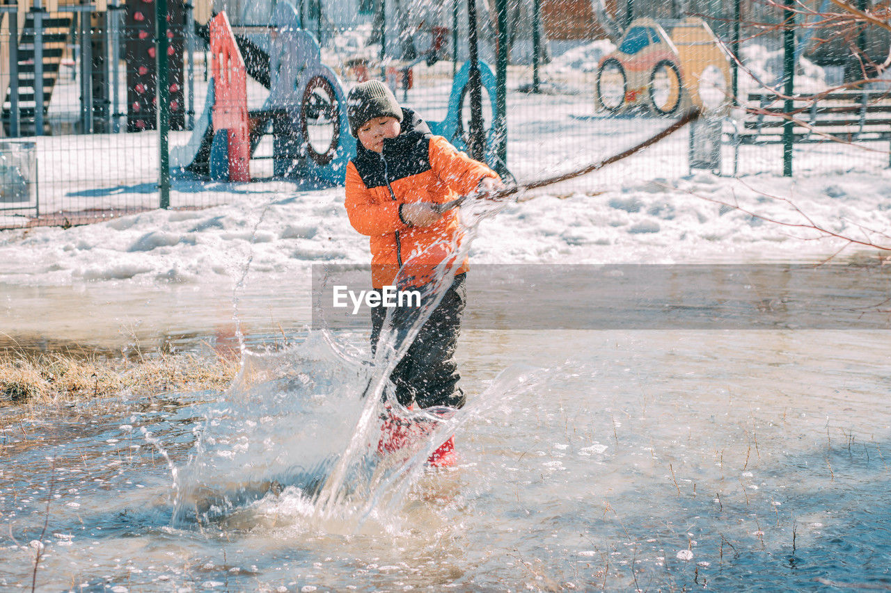 Child splashes through melting remnants of winter, shovel in hand,  joyful transition to warmer days