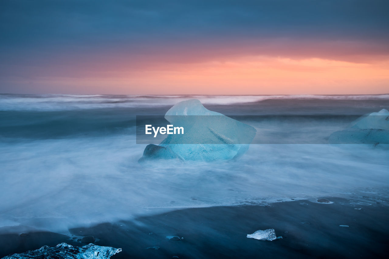 Glacier on shore against cloudy sky