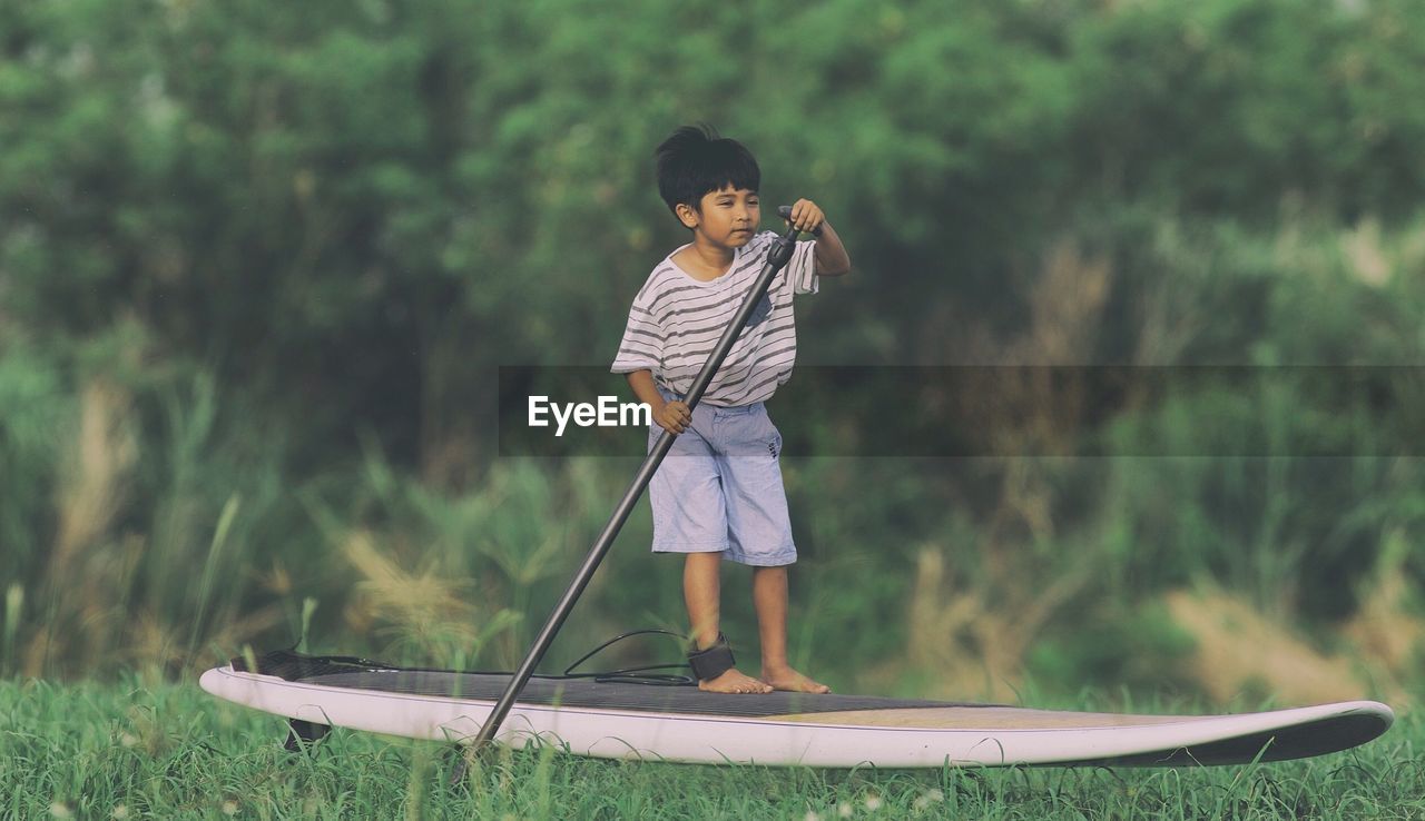 Cute boy standing on paddleboard against trees