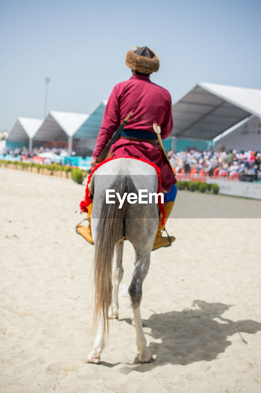 REAR VIEW OF WOMAN RIDING HORSE ON SAND