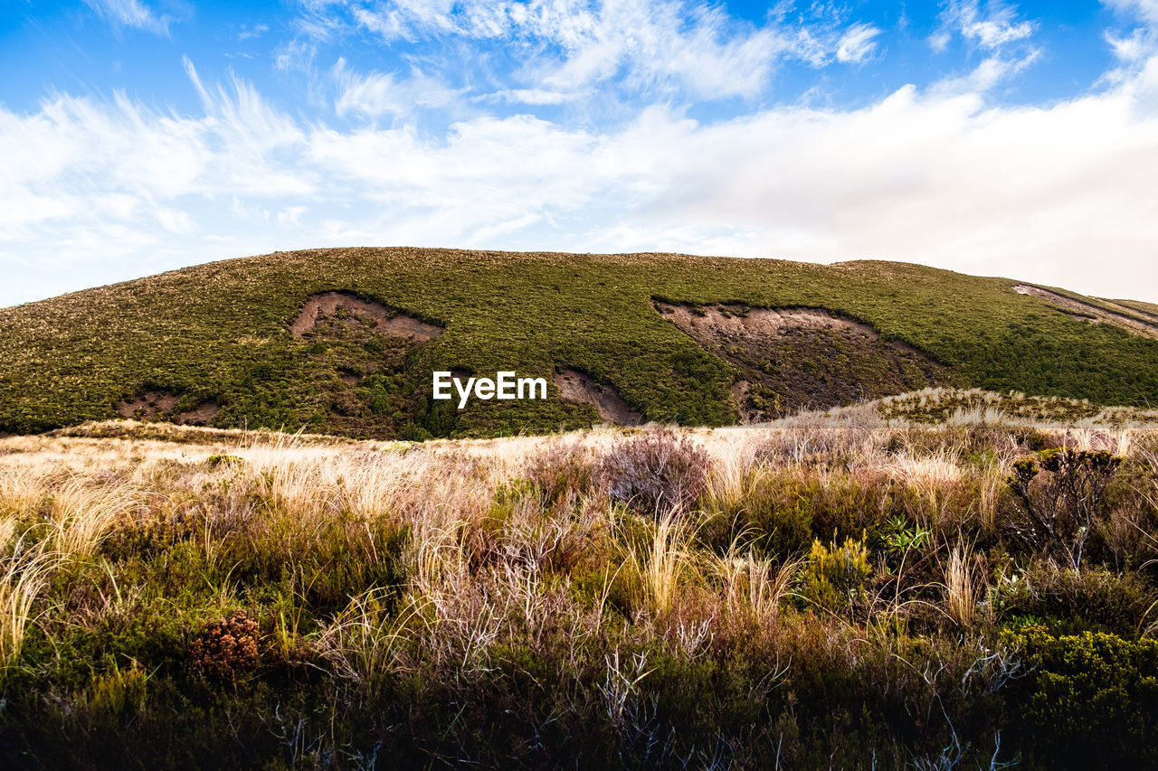 Low angle view of green mountains against cloudy sky