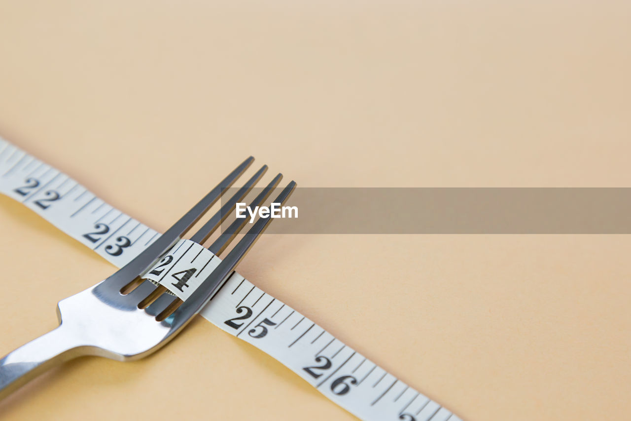 Close-up of fork with tape measure on beige background