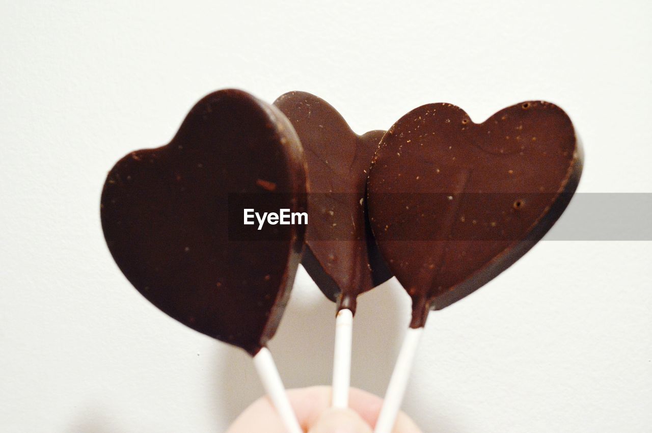 Close-up of hand holding heart shape chocolates over white background