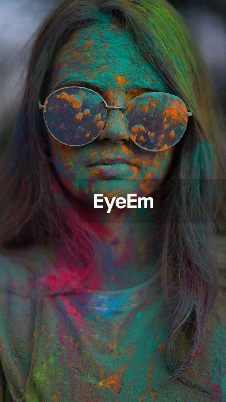 Portrait of woman standing being covered in coloured powder at holi festival.