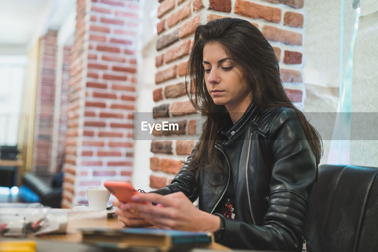 Young woman using mobile phone while sitting at cafe