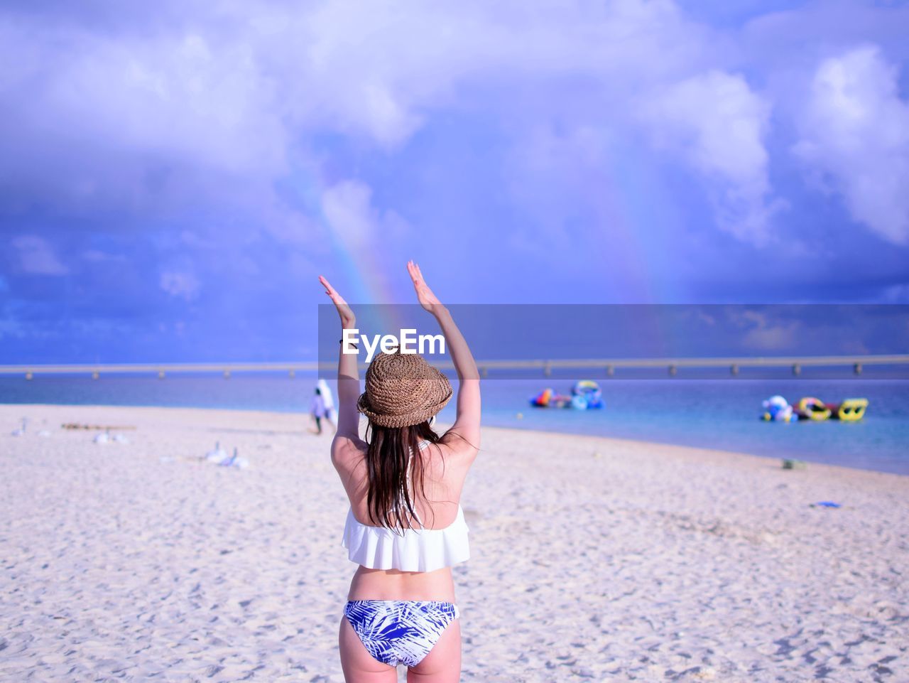 Rear view of woman gesturing while standing at beach against sky