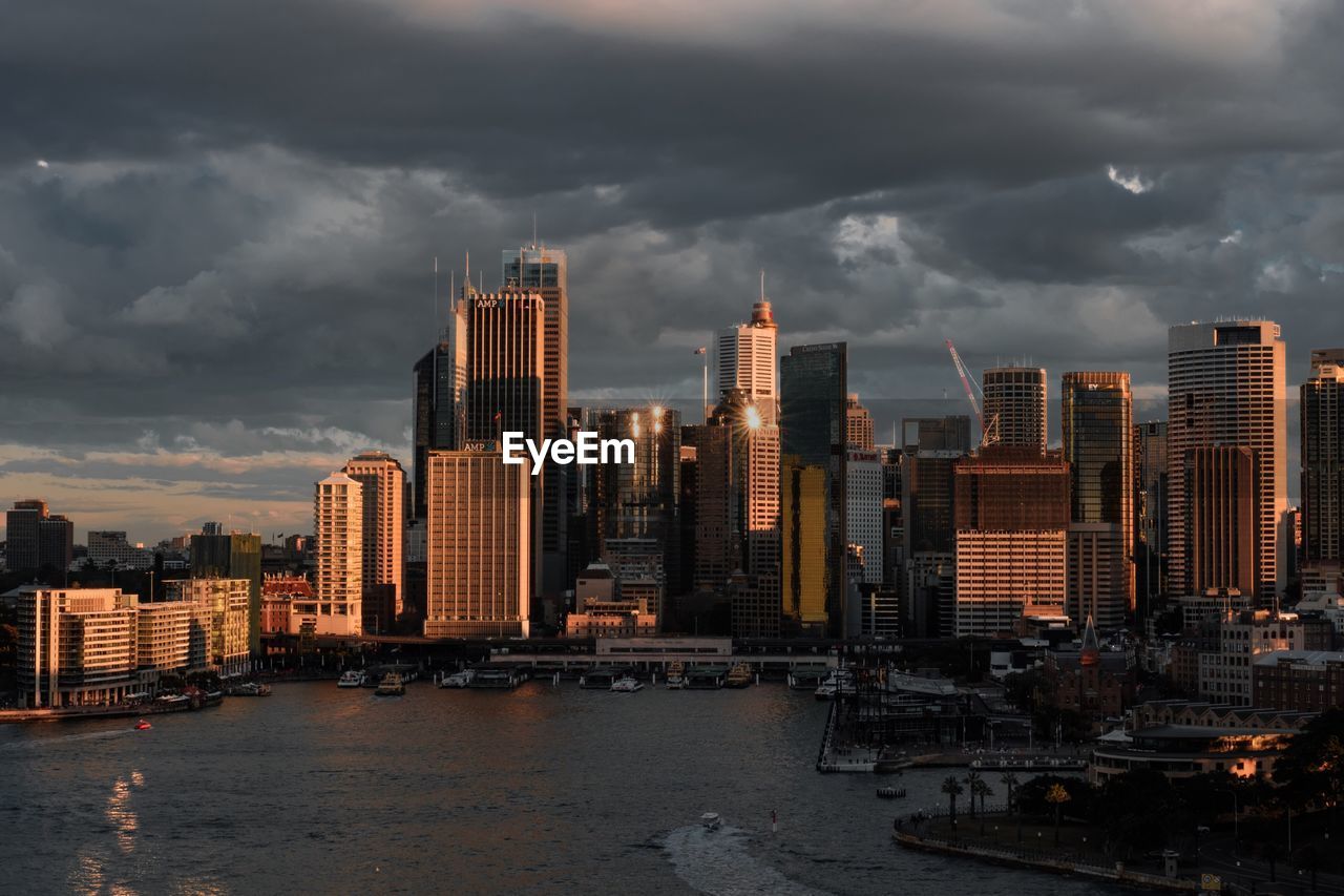 City at waterfront against cloudy sky