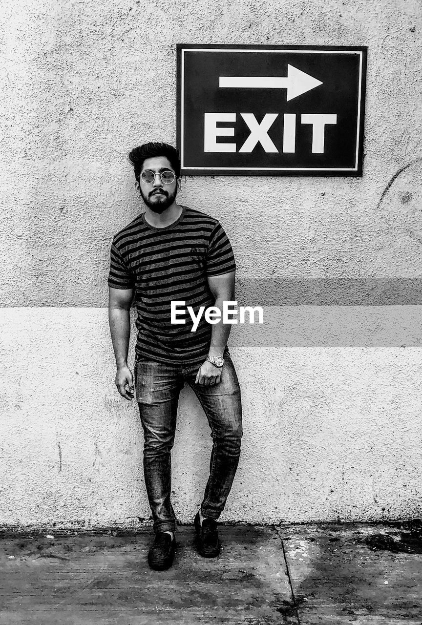 Portrait of young man standing against wall with information sign