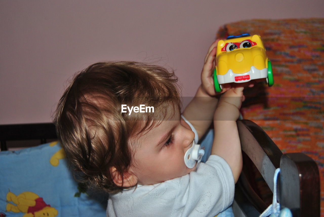 Cute baby boy sucking pacifier while playing with toy car at home