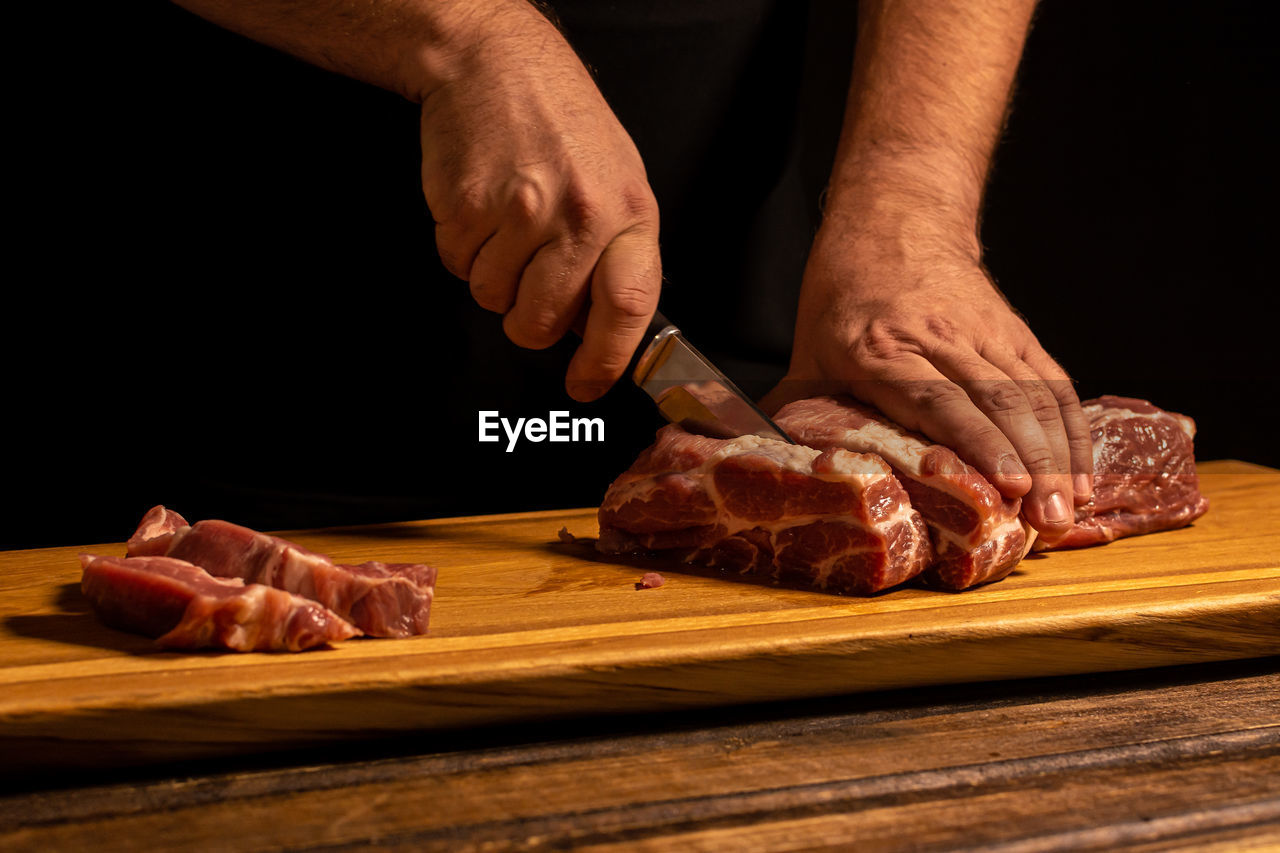 food and drink, food, meat, hand, cutting board, freshness, kitchen knife, cooking, raw food, one person, cutting, chopping, flesh, red meat, indoors, beef, goat meat, occupation, preparing food, pork, adult, men, cuisine, butcher, chef, wood, close-up, table