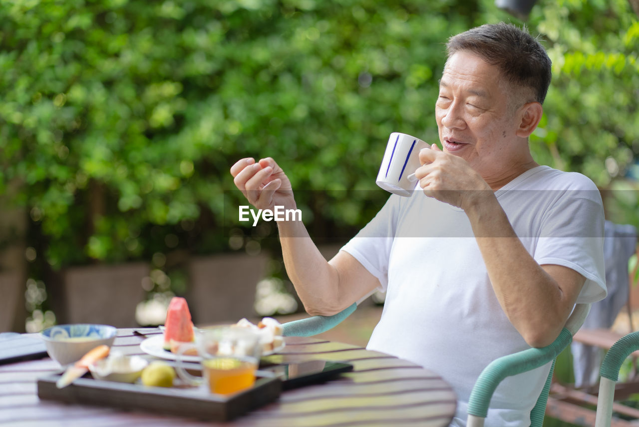 Smiling senior man drinking coffee while sitting on chair outdoors