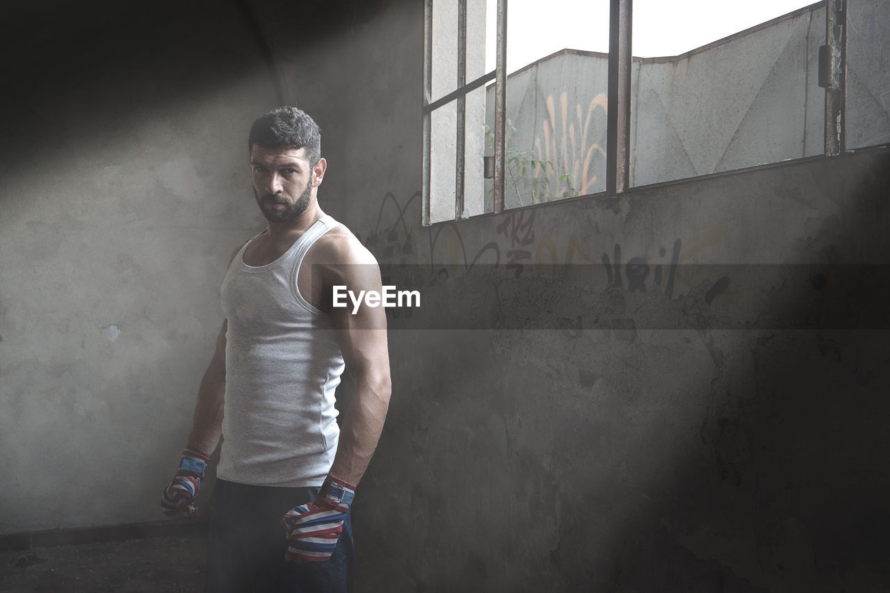 Portrait of muscular man standing against wall