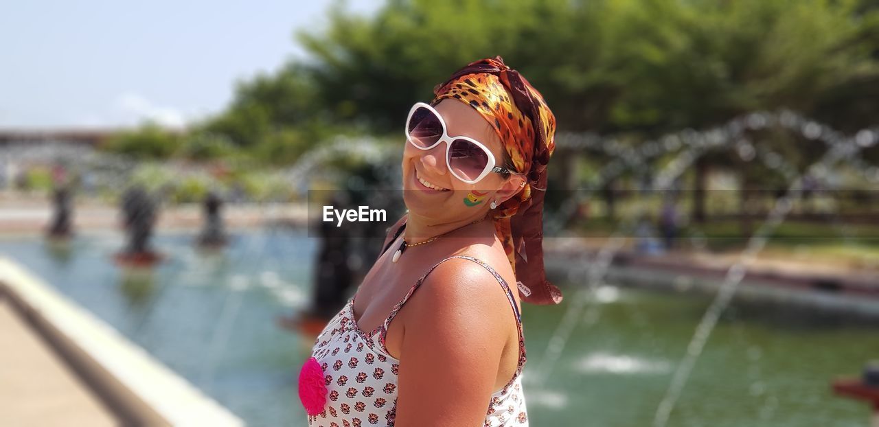 Side view portrait of smiling woman wearing sunglasses against fountain