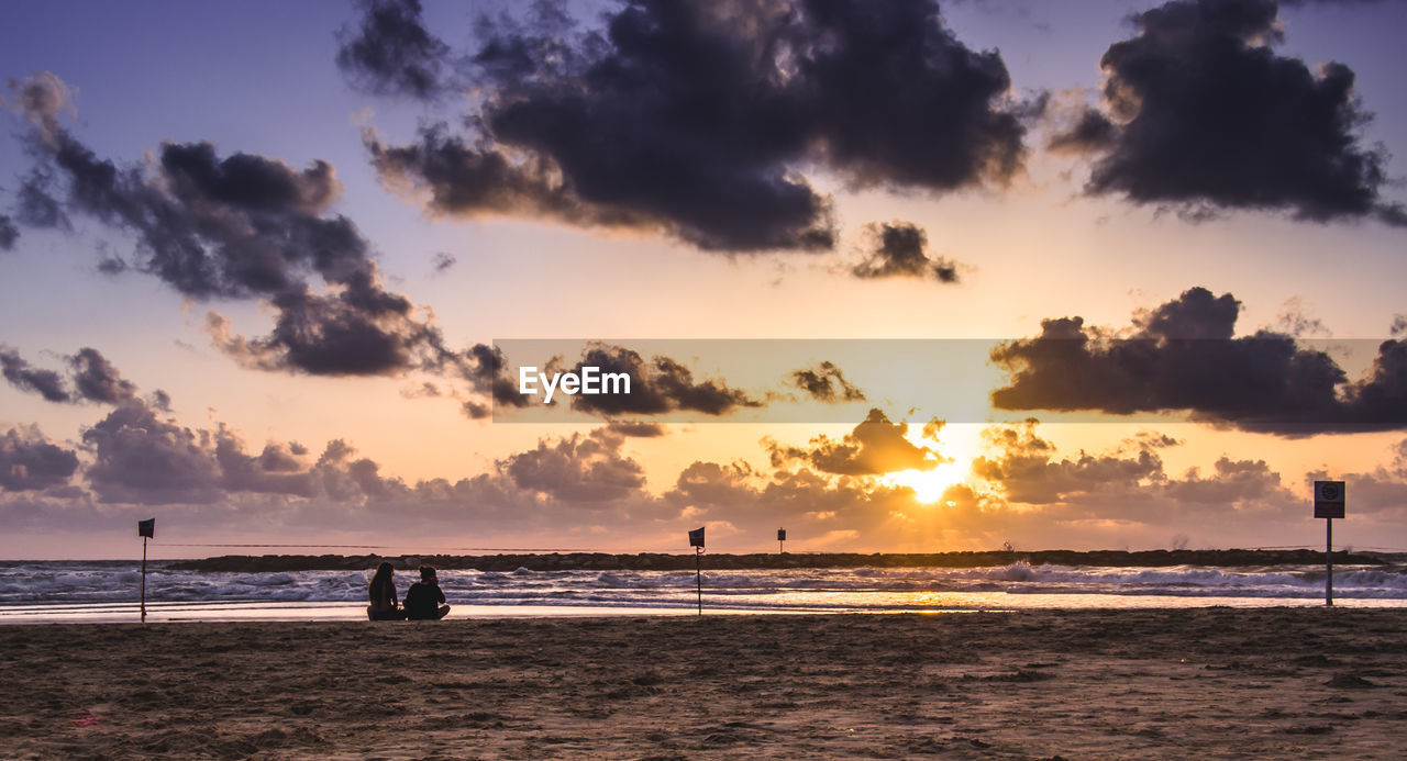 Scenic view of beach against cloudy sky during sunset