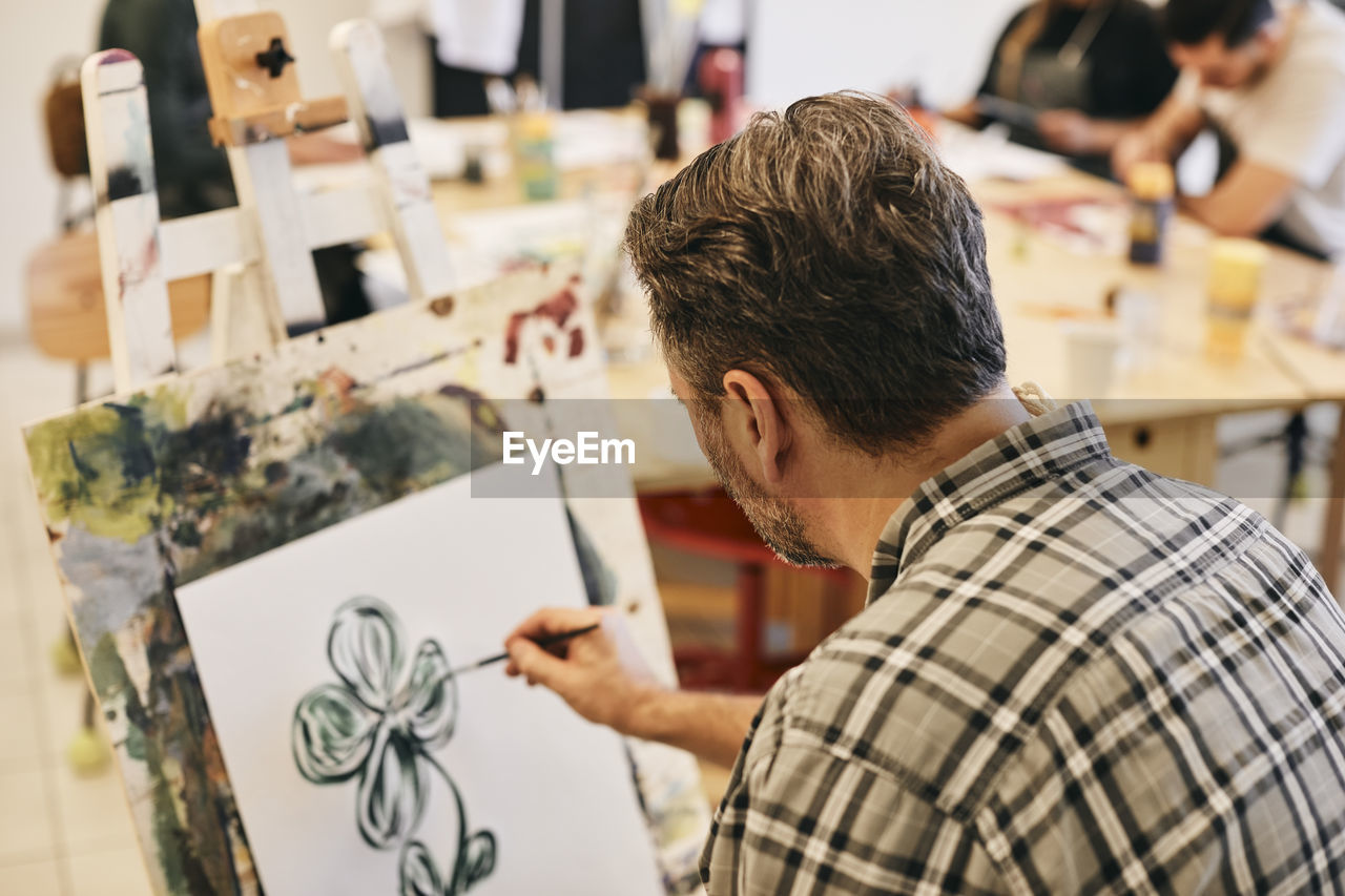 Mature male student practicing painting on artist's canvas in art class