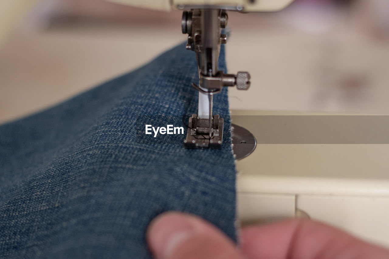 Close up of a person sewing blue jeans on a sewing machine
