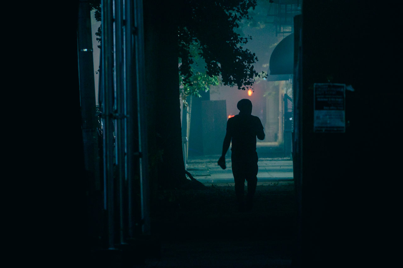 REAR VIEW OF SILHOUETTE MAN STANDING AGAINST ILLUMINATED BUILDING