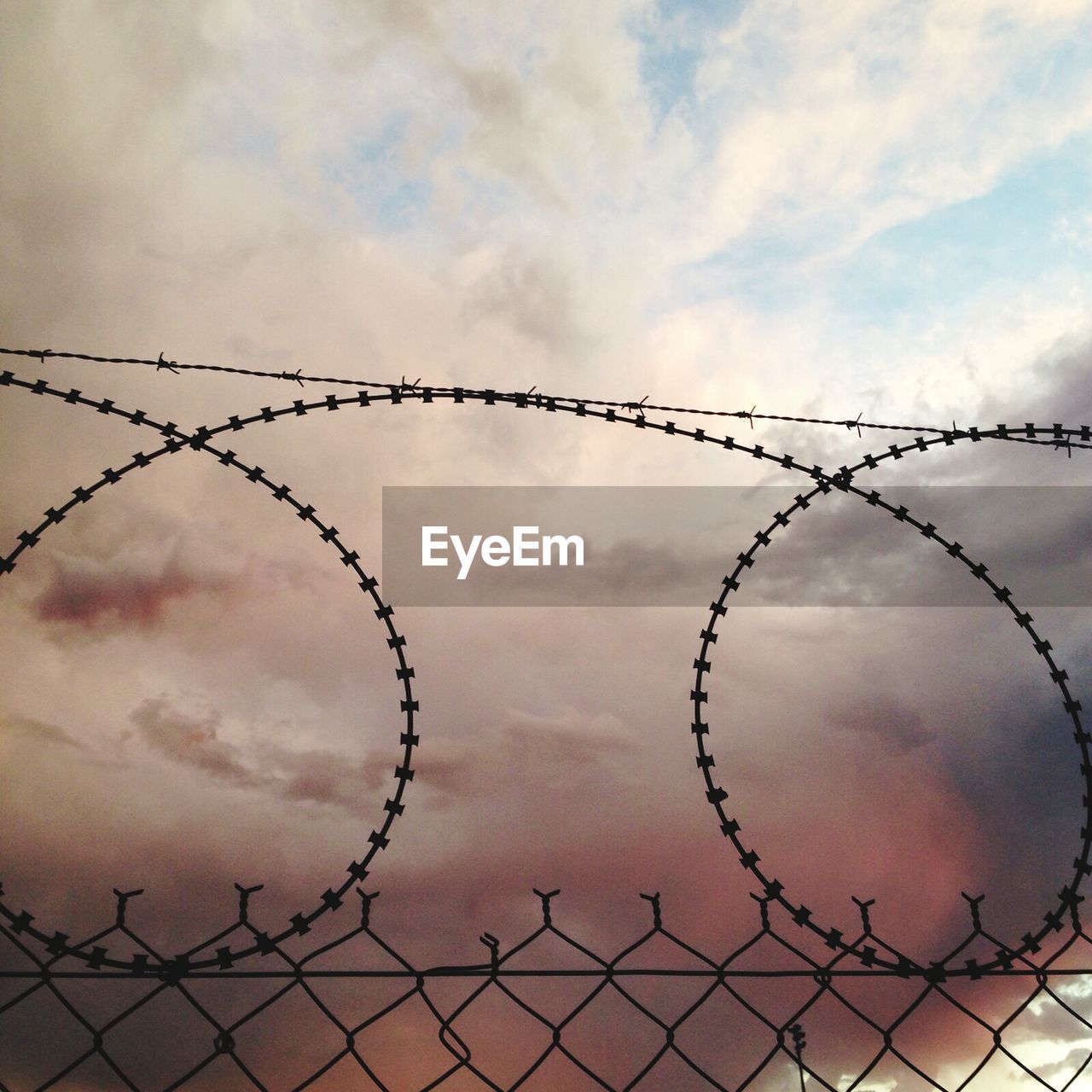 Low angle view of fence against clouds