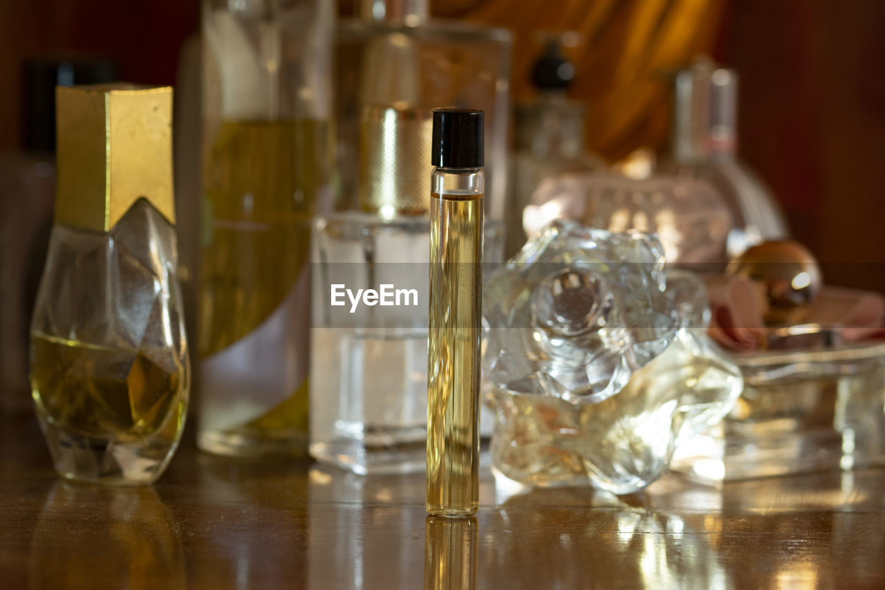 perfume, bottle, table, indoors, container, glass, food and drink, no people, alcoholic beverage, distilled beverage, drinking glass, household equipment, refreshment, drink, lighting, yellow, glass bottle, close-up, alcohol, still life