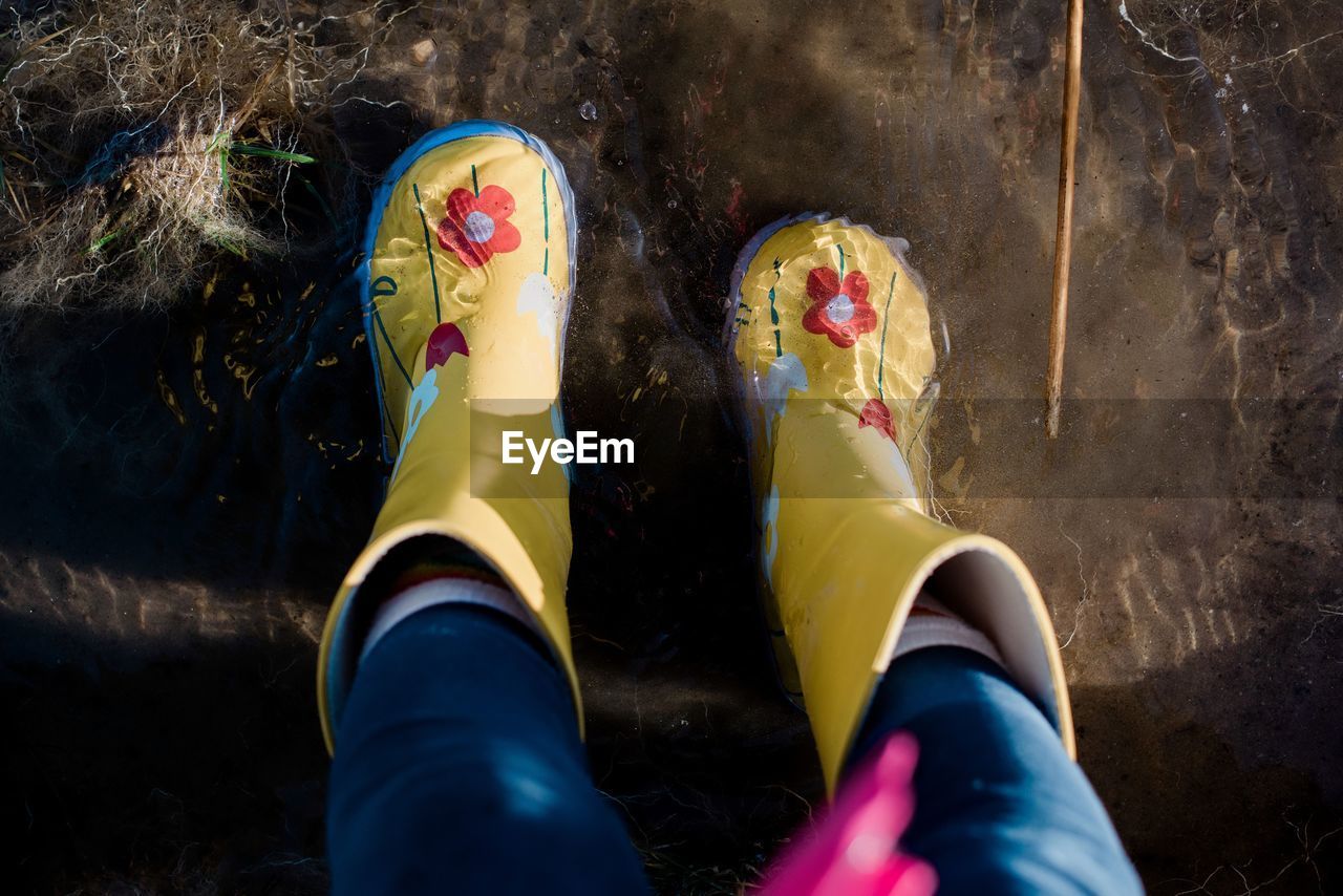 Childs feet in rain boots in a puddle of water and mud