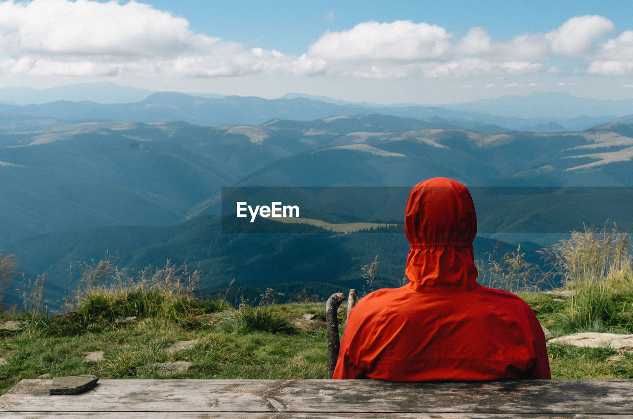 Rear view of man sitting on mountain against cloudy sky