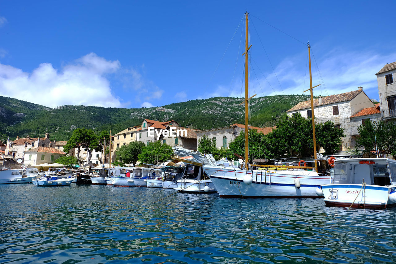 SAILBOATS MOORED IN HARBOR AGAINST SKY