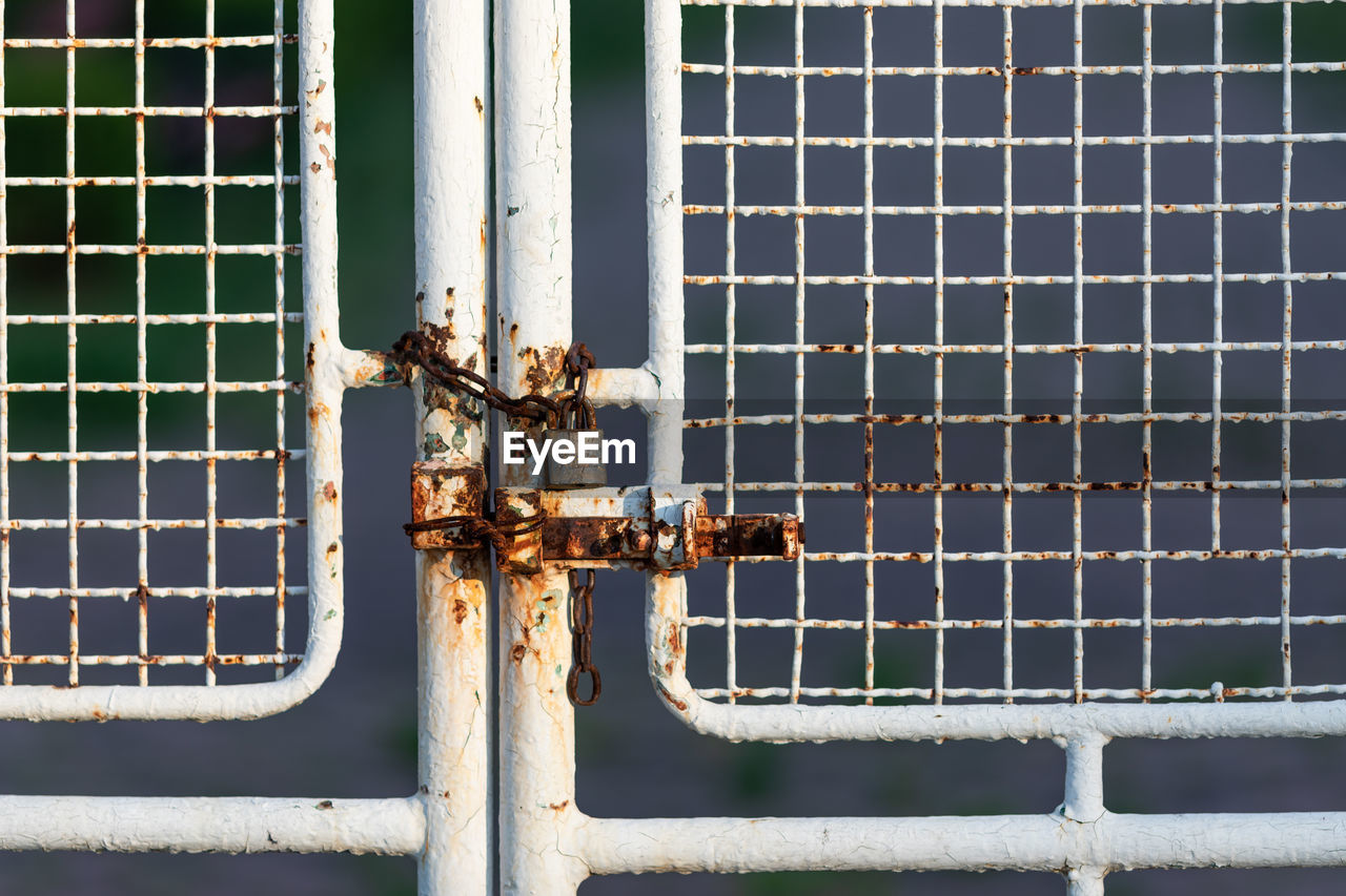 CLOSE-UP OF RUSTY METAL PIPE AGAINST GATE