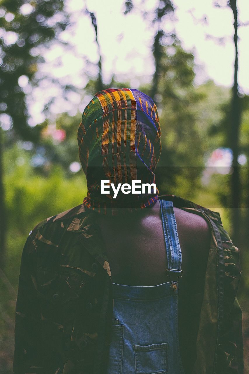 Man with covered face standing against trees in forest