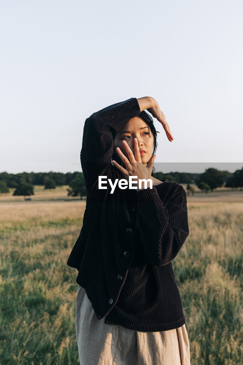 Young woman touching face while standing at park