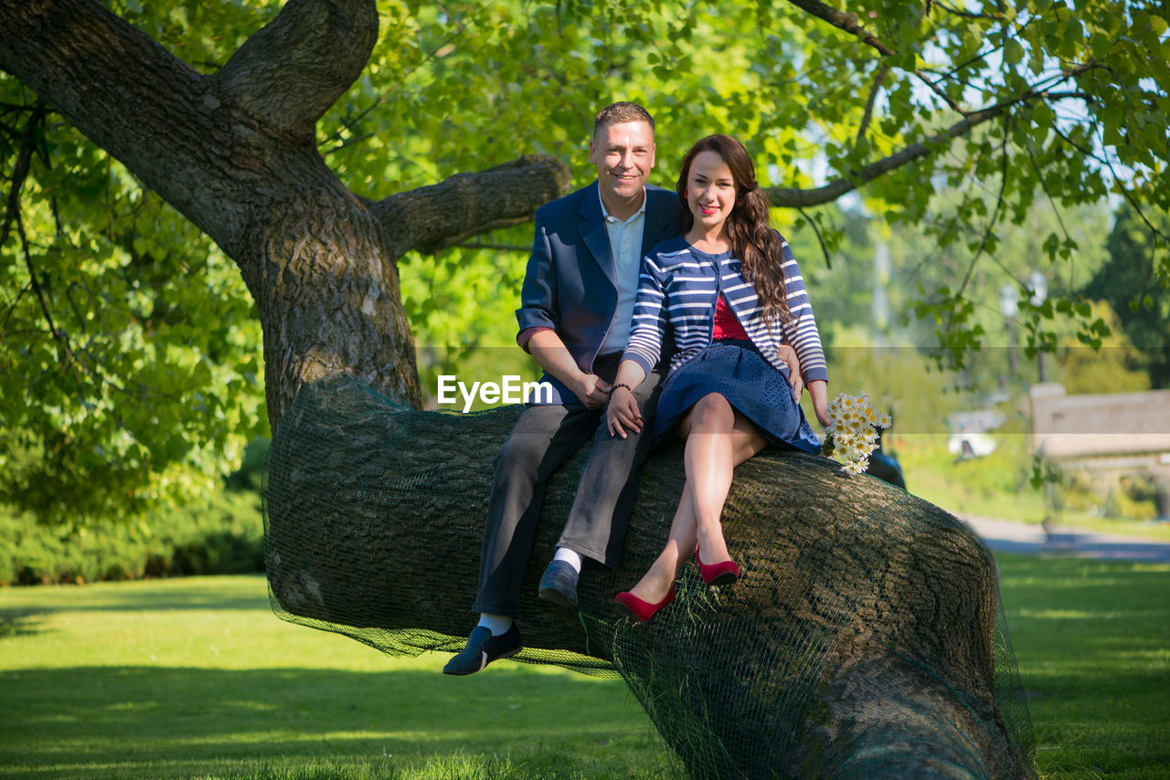 Portrait of man and woman sitting on tree trunk at park