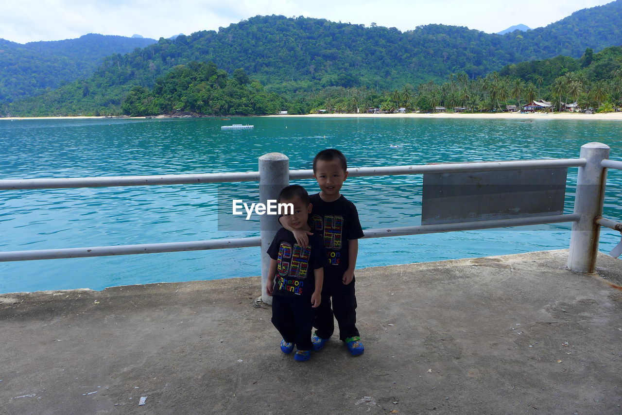 Portrait of smiling siblings standing by railing against river and mountains