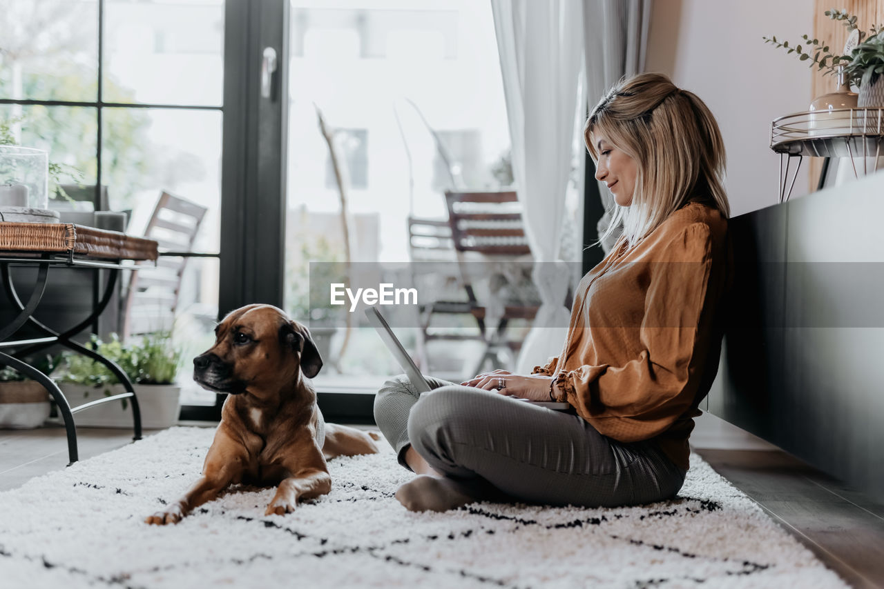 Side view of woman with dog sitting on floor at home