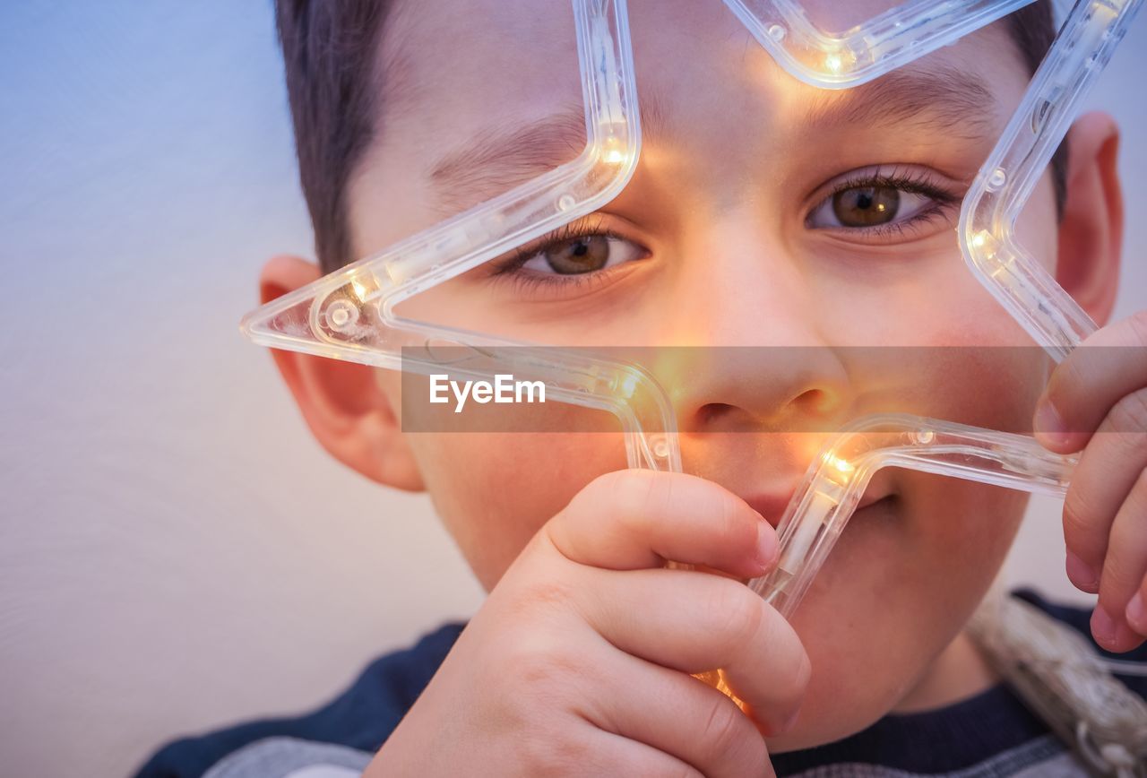 Close-up portrait of boy holding illuminated star shape