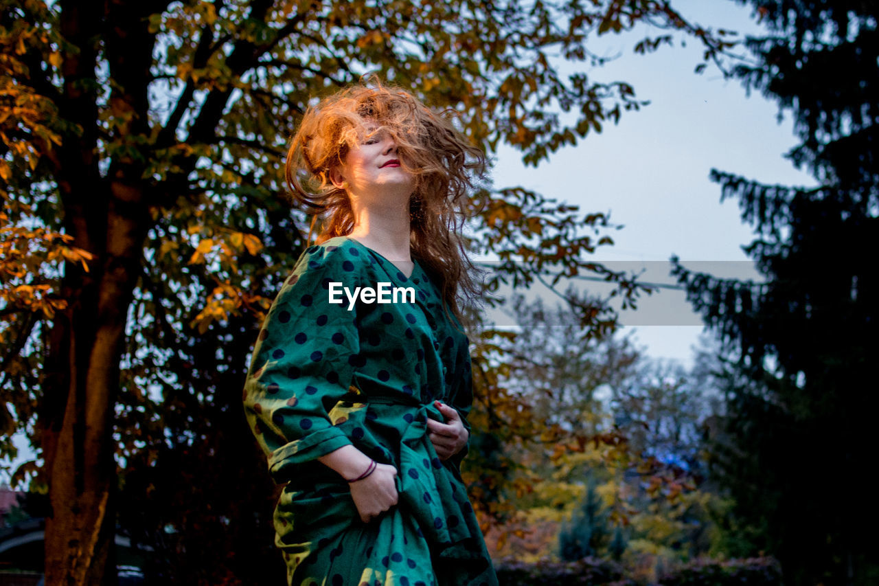 Portrait of young woman with tousled hair standing against trees