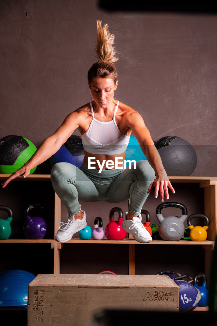 Determined athletic female in activewear jumping on wooden box while doing exercises in modern gym during training