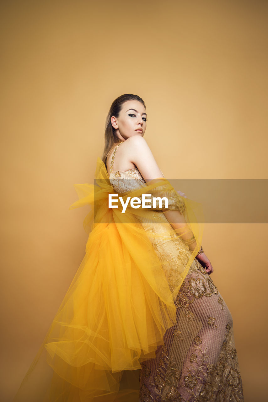 PORTRAIT OF BEAUTIFUL YOUNG WOMAN AGAINST YELLOW BACKGROUND