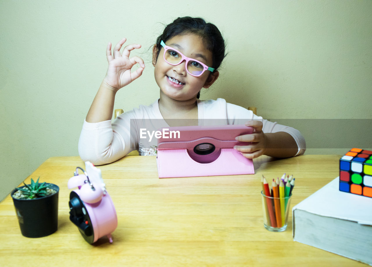 PORTRAIT OF GIRL HOLDING EYEGLASSES ON TABLE