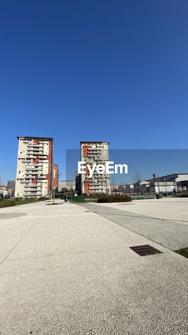 STREET BY BUILDINGS AGAINST CLEAR BLUE SKY