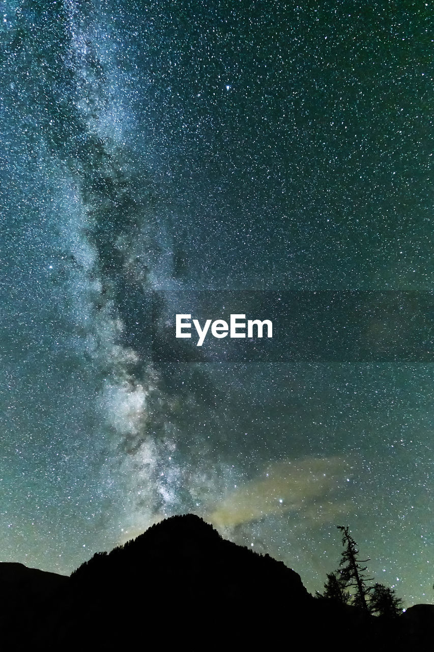 Low angle view of galaxy over silhouette mountain at night