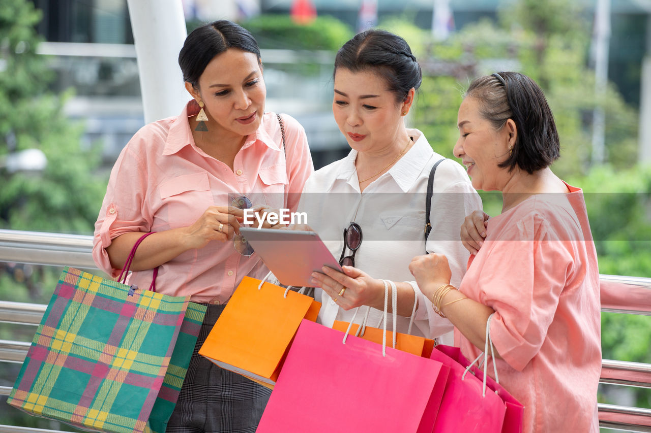 Smiling women using digital tablet while holding shopping bags