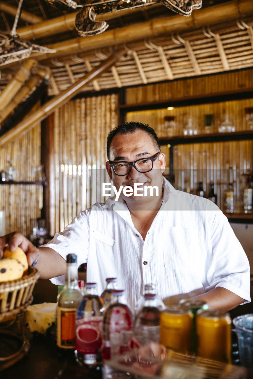 Portrait of smiling bartender with eyeglasses at counter in resort