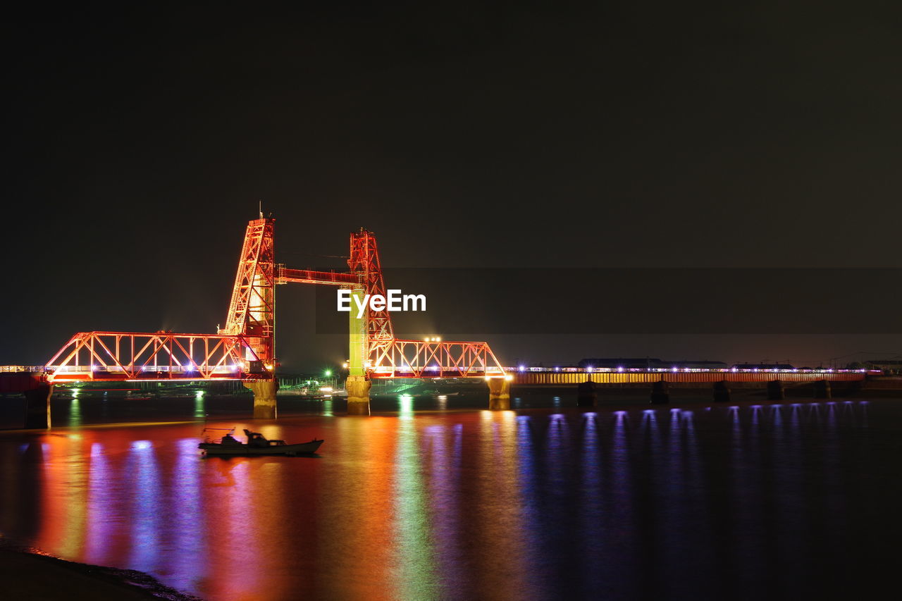 Illuminated bridge over river against sky at night