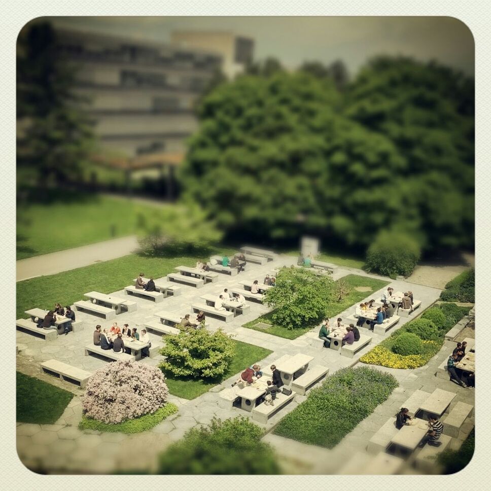 Tilt-shift of people sitting on stone bench for lunch in formal garden